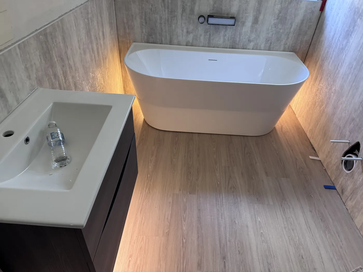 Freestanding bath with LED plinth lighting and a dark floating vanity in a newly fitted loft bathroom with wood-effect flooring.