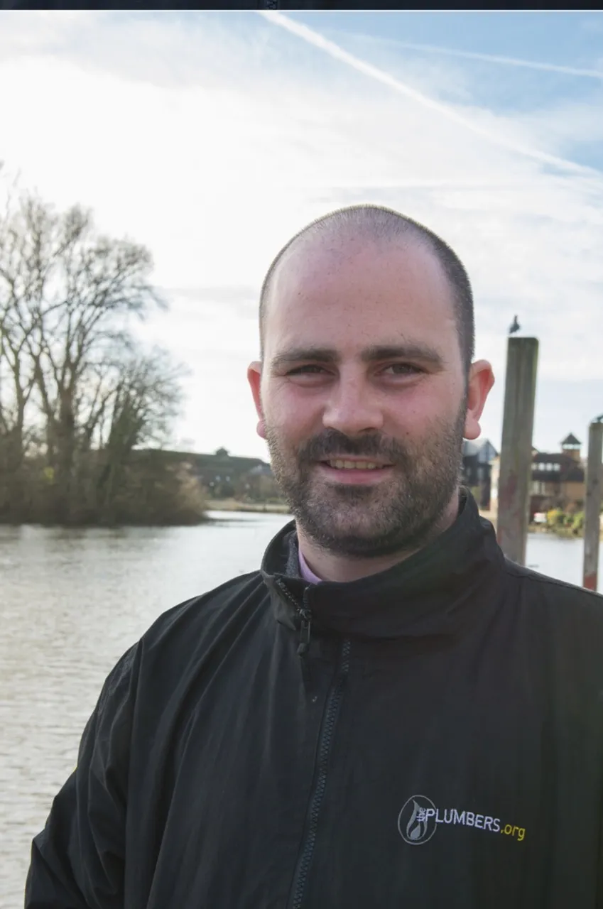 Senior plumbing and heating engineer in ThePlumbers.org branded jacket photographed riverside in West London.
