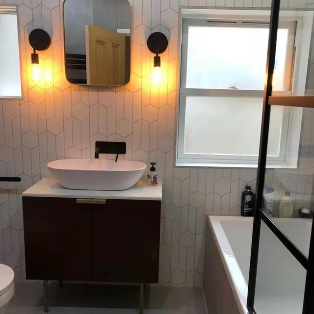 Boutique-style bathroom with hexagon feature tiles, industrial wall lights, countertop basin on a walnut washstand and black fittings.