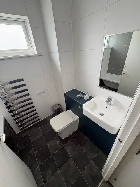 Compact modern bathroom with navy vanity unit, square basin, black towel radiator, mirrored cabinet and dark slate-effect floor tiles.