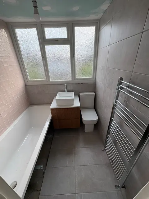 Refitted bathroom with blush pink metro wall tiles, walnut vanity with countertop basin, new bath and chrome heated towel rail.
