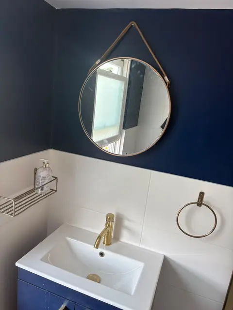 Navy blue bathroom wall with brushed brass tap, round hanging mirror and white basin vanity in a refurbished London bathroom.