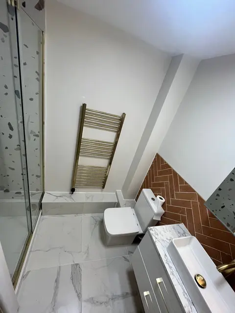 En-suite shower room with terracotta herringbone feature tiles, marble floor, gold tap and white countertop basin.