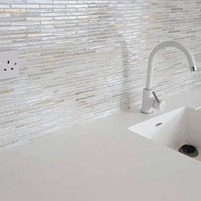 Kitchen refurbishment with white composite sink, curved mixer tap and glass mosaic splashback tiling.