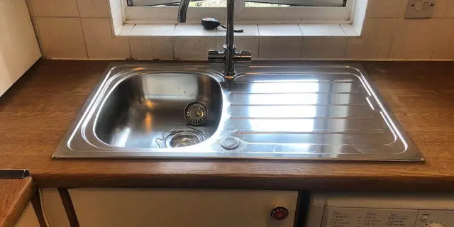 Replacement stainless steel kitchen sink and mixer tap fitted into a solid wood worktop.