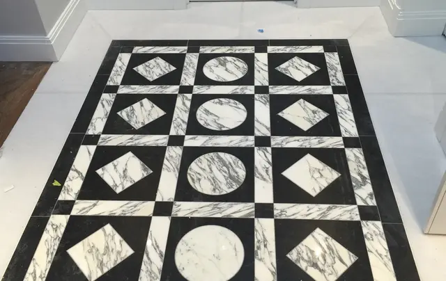 Bespoke black-and-white marble floor with circle and diamond inlays being laid during a luxury renovation project.