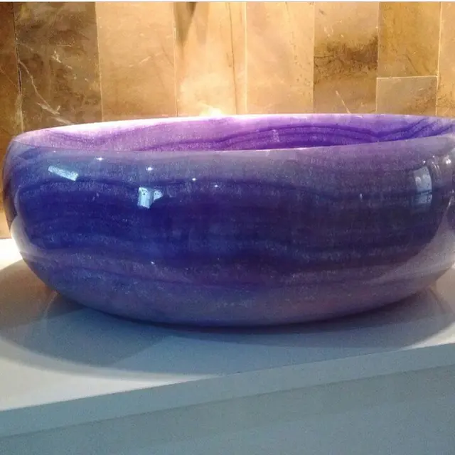 Polished purple onyx vessel basin installed in a marble-tiled bathroom as a statement feature.