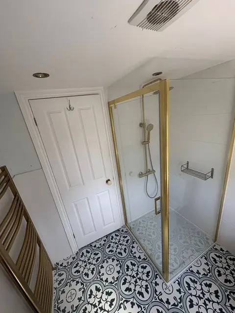 Brushed brass shower enclosure and heated towel rail with black-and-white patterned Victorian-style floor tiles in a renovated bathroom.
