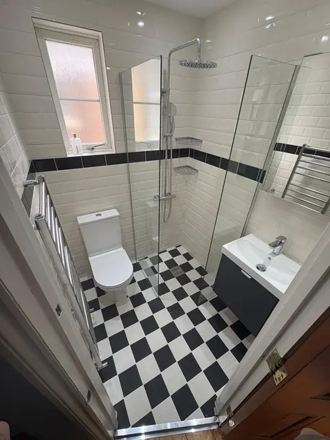 Traditional-style shower room with black-and-white chequerboard floor, white metro tiles with black border and corner glass shower.
