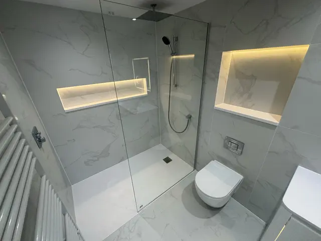 Walk-in rainfall shower in large-format marble-effect tiles with a full-width LED-lit niche and frameless glass screen.
