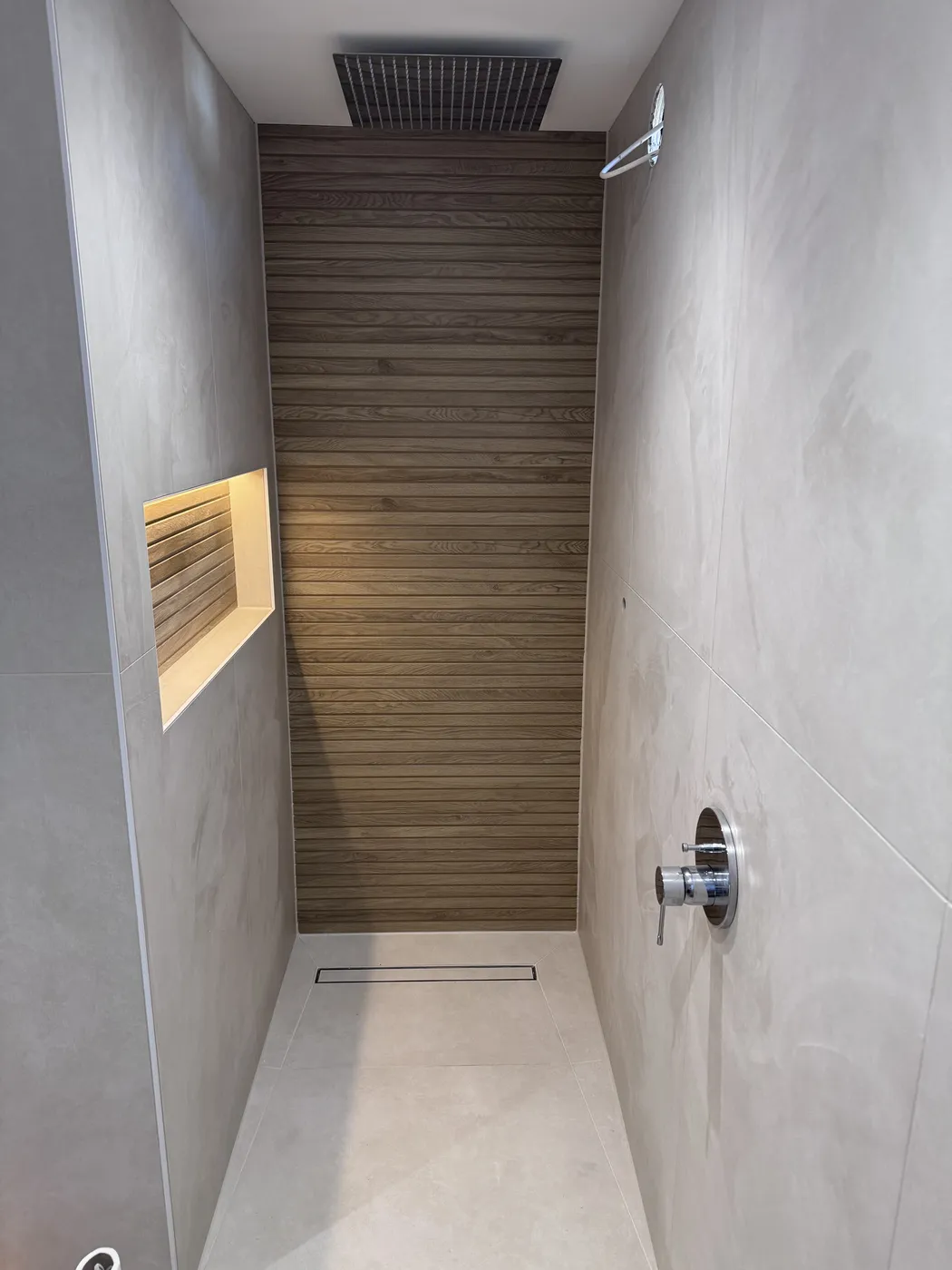 Wet-room style walk-in shower with ceiling-mounted rainfall head, wood-look feature wall, LED-lit storage niche and linear drain.